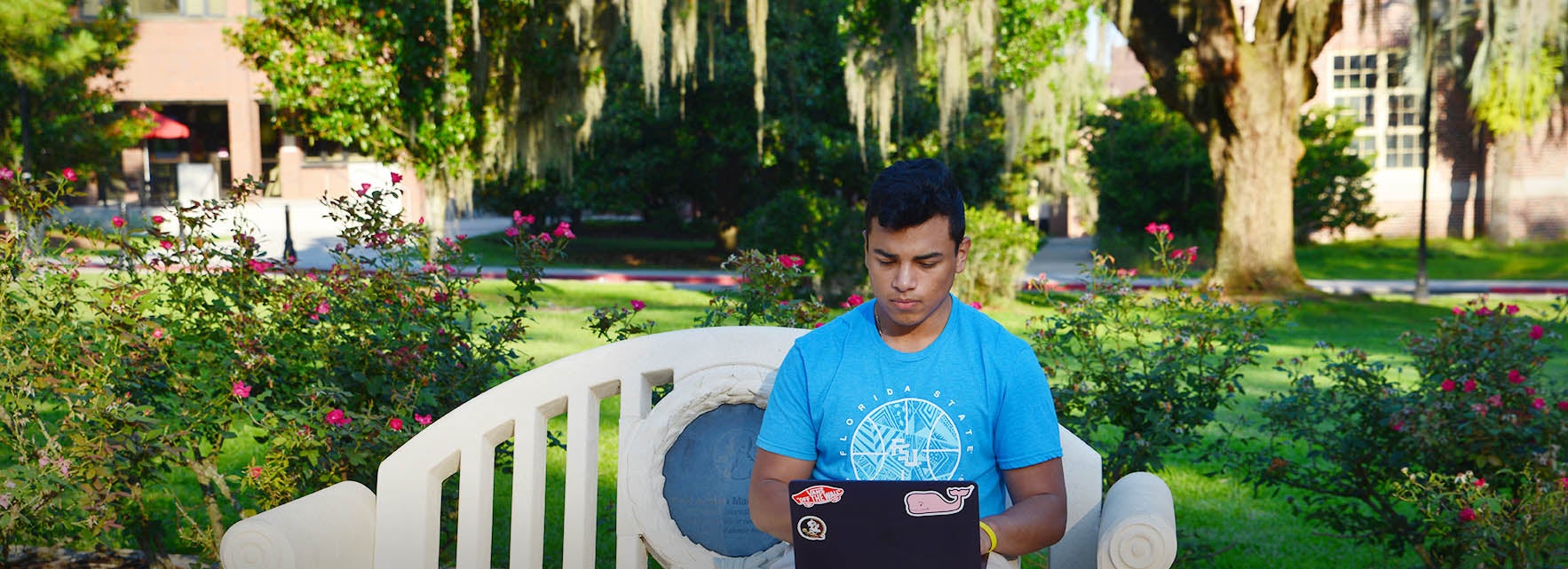 An FSU student works on a laptop while seated on a bench.